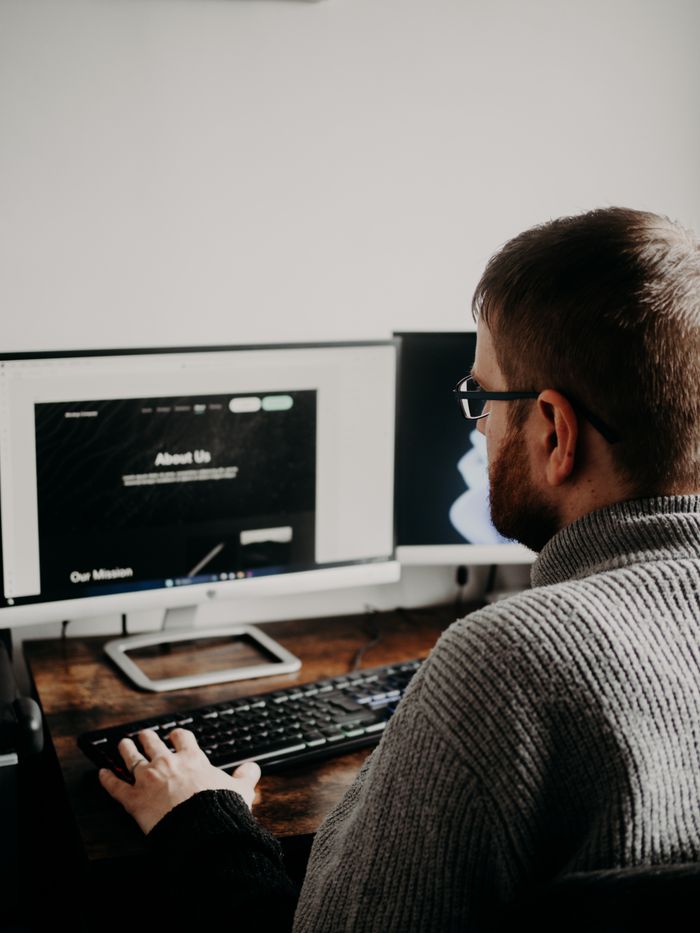 Services Man working on web design at home office setup with dual monitors.