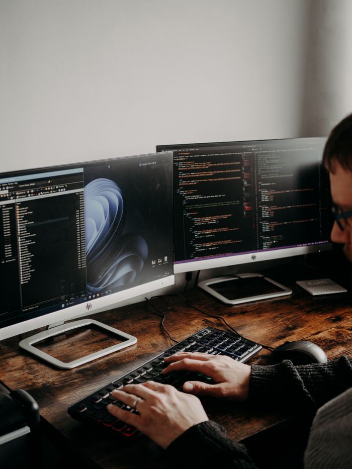 About A man working on website design and coding at a home office with a dual monitor setup.
