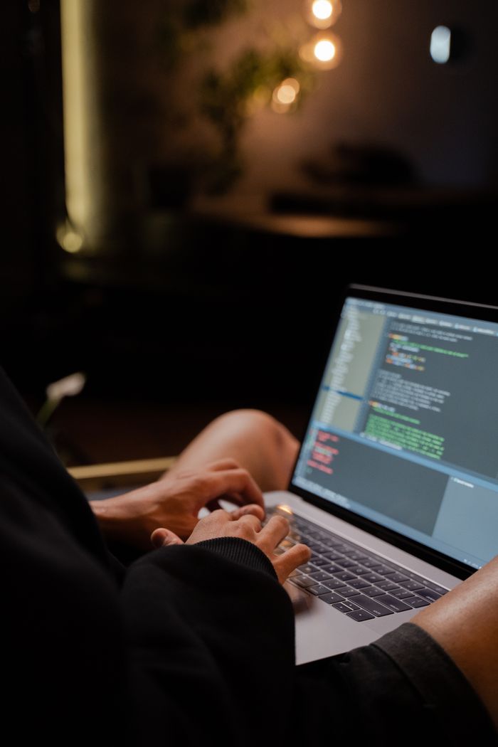 About Focused hands typing code on a laptop in a dimly lit room, showcasing programming activities.